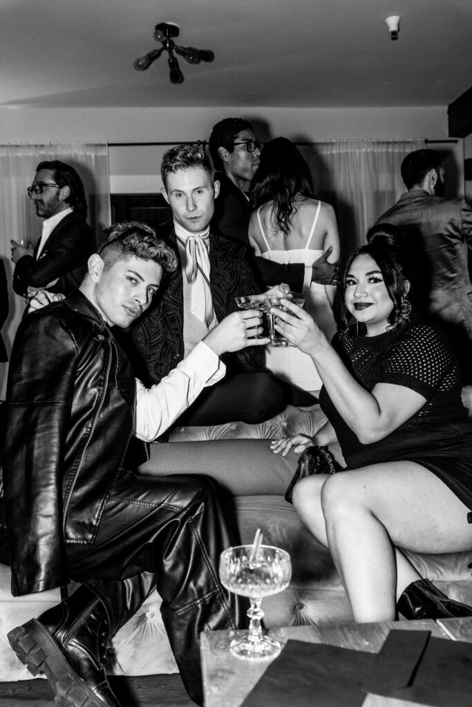 martin silva kyle fedasiuk and gabi villalta sitting on a couch cheersing glasses in black and white at arizona's fashion industry night at parsons villas for luxe and city and arizona fashion week